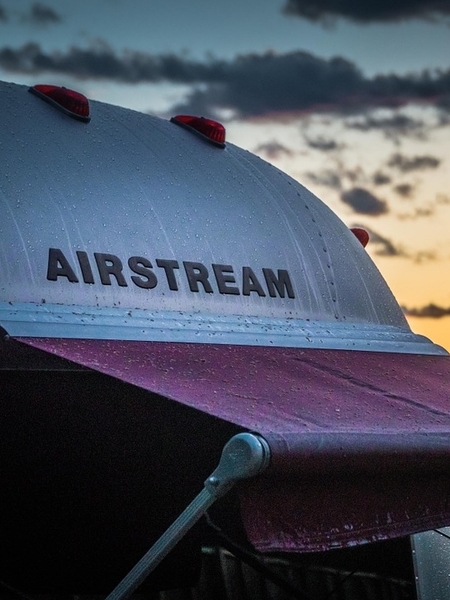 Airstream® camper with open awning parked outside with a sunset in the background